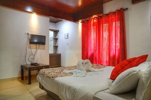 A hotel room with a bed, a TV mounted on the wall, and a red curtain. - Vythiri Wild Forest Resort (Vythiri)