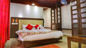 A hotel room with a bed, a bedside table, a chair, and a fan. - Vythiri Wild Forest Resort (Vythiri)