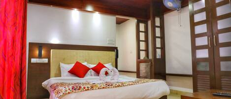 A hotel room with a bed, a bedside table, a chair, and a fan.