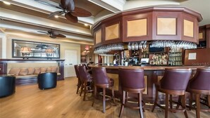A bar area with a curved counter, multiple bar stools, and a ceiling fan. - Heritage Oaks 2 Bedroom with Golf Course and Water Views (Sarasota)