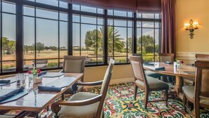 A dining area with large windows, a patterned carpet, and a table set for two. - Heritage Oaks 2 Bedroom with Golf Course and Water Views (Sarasota)