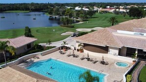 A resort with a swimming pool, lounge chairs, and a golf course in the background. - Heritage Oaks 2 Bedroom with Golf Course and Water Views (Sarasota)