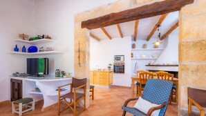 Una cocina rústica con vigas de madera, un comedor con sillas y un televisor sobre una mesa blanca.
