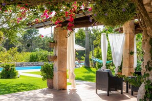 Ein überdachter Außenbereich mit Pool, Pflanzen und Gartenmöbeln.