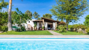 Vista de una piscina con una casa, un patio, una hamaca y un jardín.