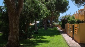 Un chemin bordé d’arbres et une façade jaune mènent à un bâtiment dont l’entrée est ornée de carreaux.