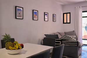 Una habitación con una mesa de comedor, un frutero, un sofá y una ventana con cortinas.