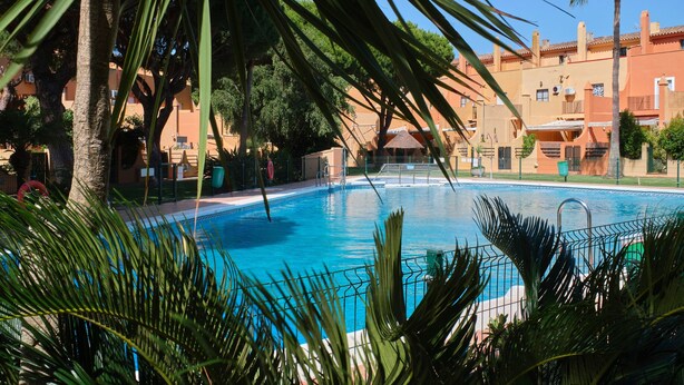 Une piscine entourée de palmiers et de bâtiments de style architectural méditerranéen.