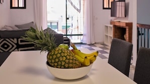 Un coin repas avec une table sur laquelle se trouve un saladier rempli de fruits, un canapé et un téléviseur.
