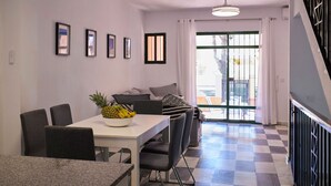 Un coin repas avec une table, des chaises et un panier de fruits. Un escalier avec une rampe se trouve sur le côté droit.