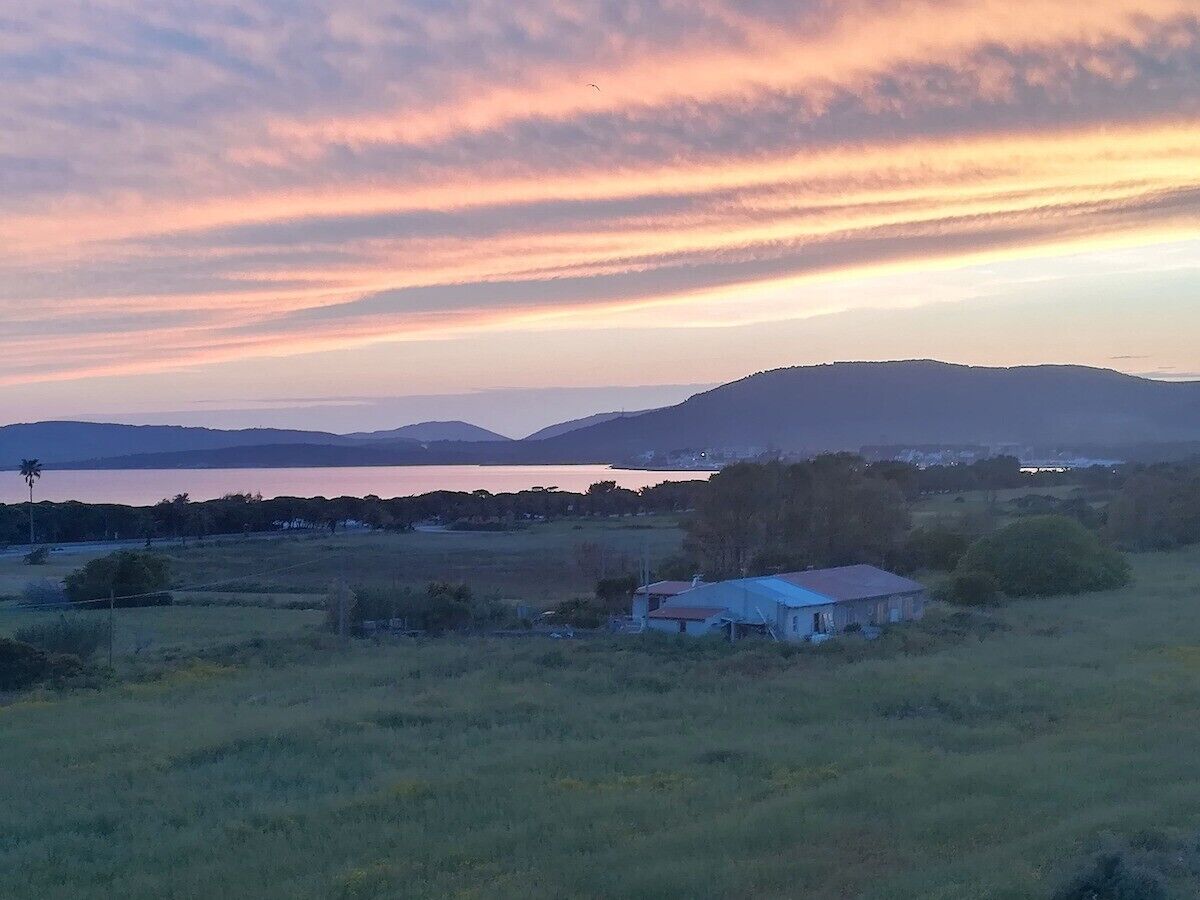 Un paysage rural avec une petite maison, de vastes champs et des collines à l’horizon.