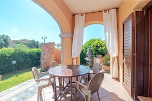 An outdoor patio with a round table and chairs, a stone wall, and a view of greenery.