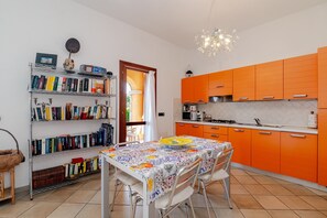 A kitchen with orange cabinets, a dining table with chairs, a bookshelf, and a chandelier.