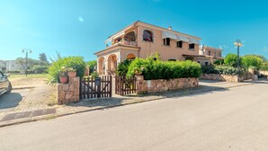Une maison à deux étages avec un mur en pierre, une entrée fermée par un portail et un ciel d’un bleu limpide.