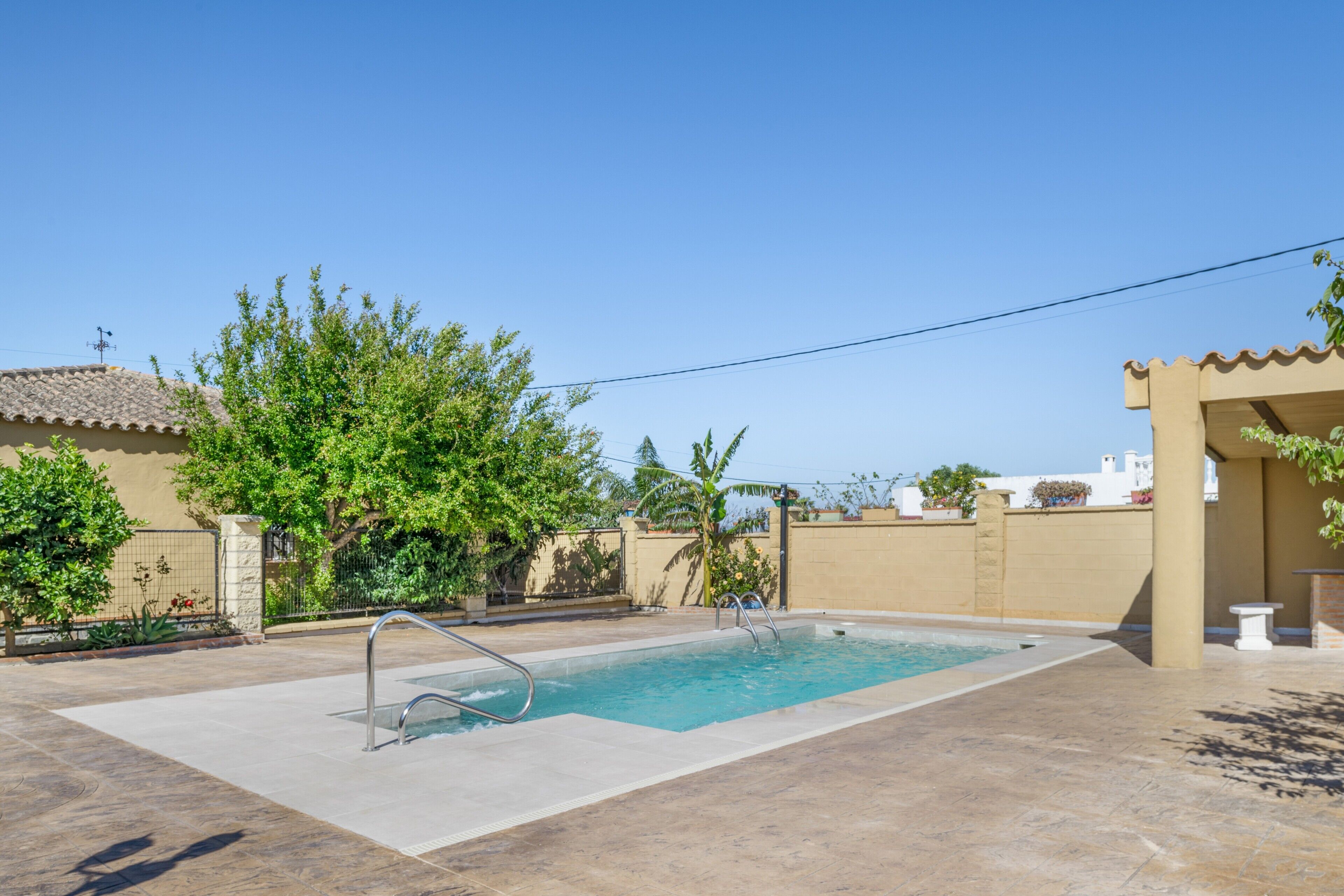A rectangular swimming pool with a metal ladder, surrounded by a tiled patio.