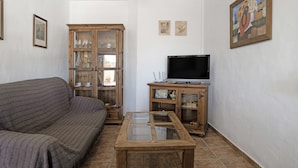 Ein Wohnzimmer mit einer Couch, einer Holztruhe mit Glastüren, einem Fernseher auf einem Holzständer und einem Gemälde an der Wand.