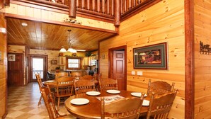 A wooden cabin interior with a dining area featuring a round table and chairs, a kitchen area, and a framed picture on the wall. - Splash N' Play #524 (Cosby)