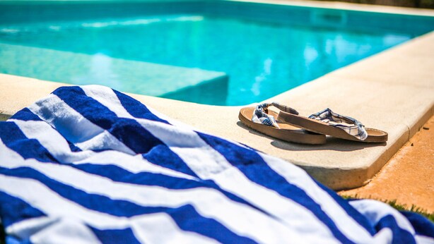 Un área junto a la piscina con una toalla azul y blanca a rayas y un par de sandalias.