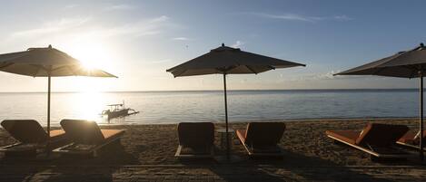 Ein Strandloungebereich mit Liegestühlen und Sonnenschirmen mit Blick aufs Meer.