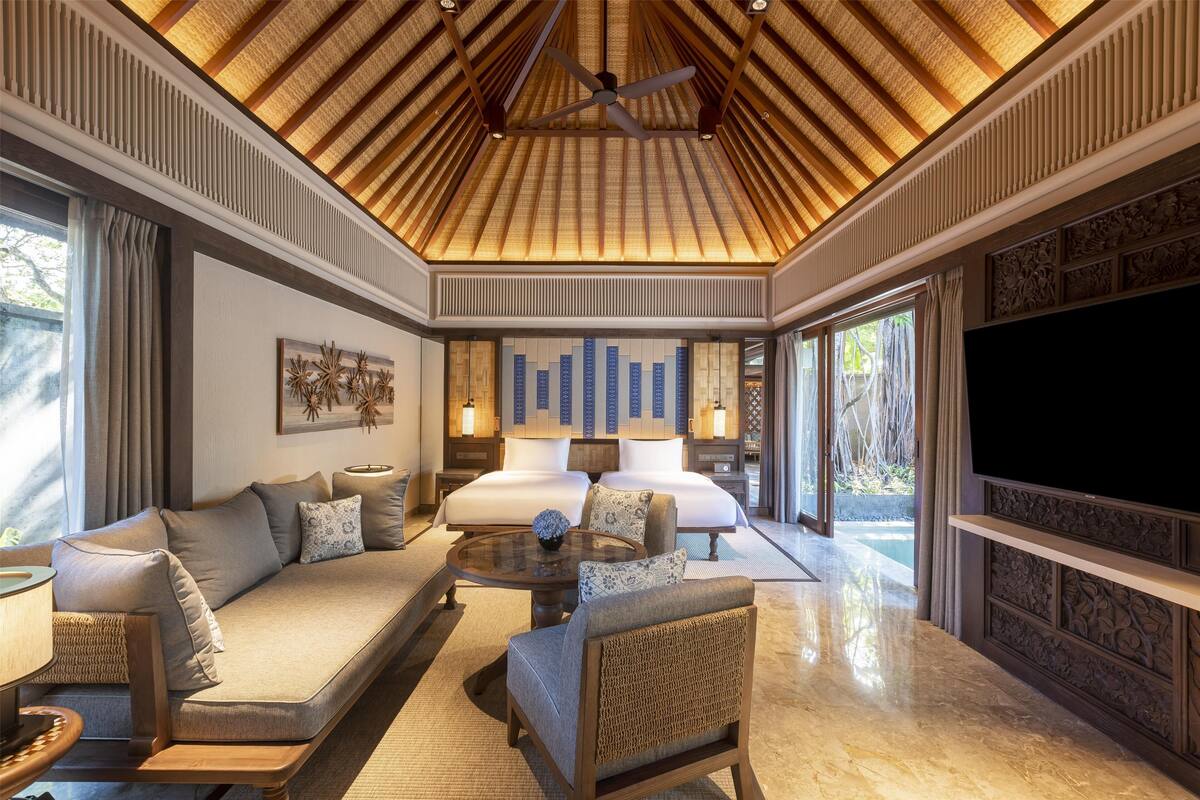 A spacious bedroom with a large bed, a sitting area with a sofa and armchairs, a ceiling fan, and a TV.