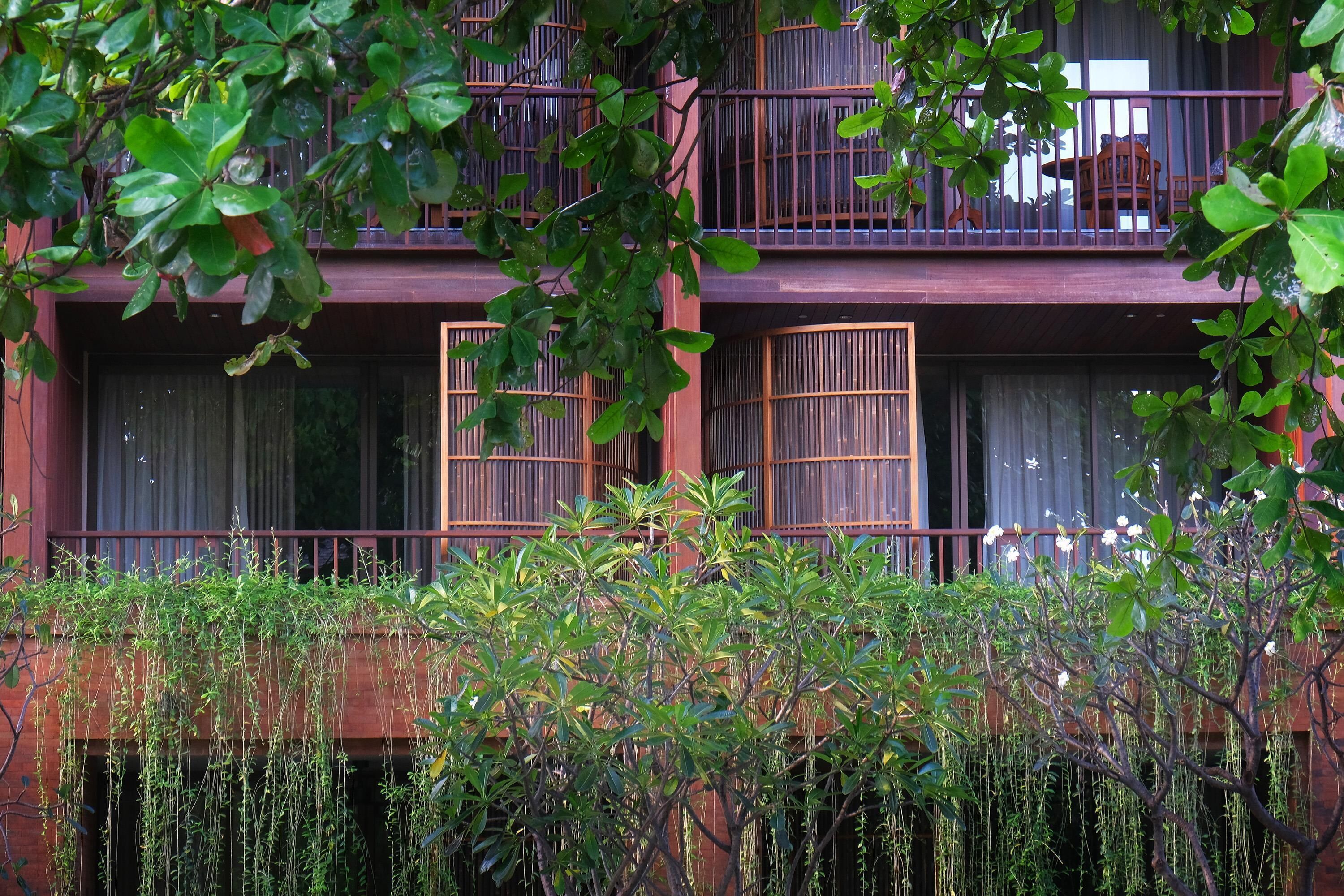 Un edificio de varios pisos con balcones, ventanas amplias y abundante vegetación al frente.