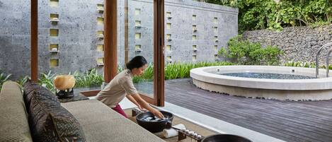 Un espacio de spa con una persona relajándose en un sofá, una bañera de hidromasaje y una pared de piedra con pequeñas repisas.
