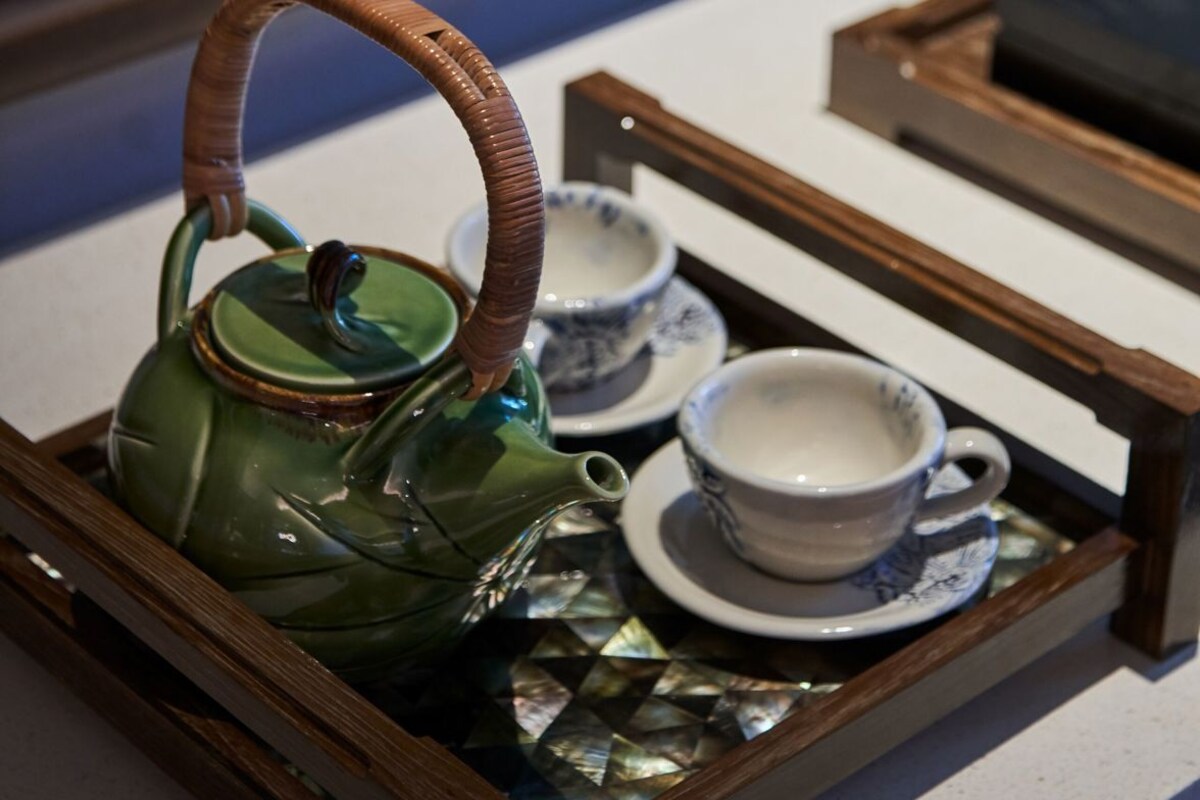 A tray with a green teapot, two blue cups, and saucers on a wooden surface.