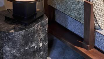 A lamp on a dark stone base, a wooden bench, and a patterned cushion on a couch.