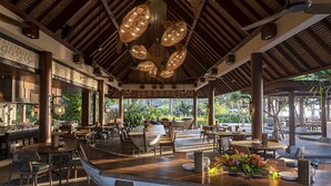 An open-air restaurant with wooden tables and chairs, a boat-shaped counter, and hanging light fixtures. - ANDAZ BALI, BY HYATT (Denpasar)