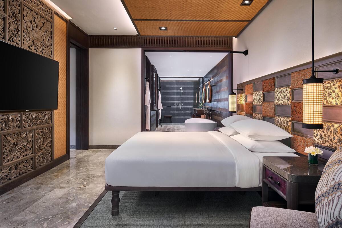 A modern hotel room with a large bed, a flat-screen TV, a bathroom with a shower, and a view of the city.