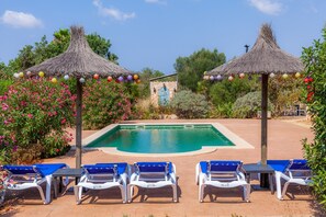 Une piscine dotée de chaises longues et de parasols en chaume.