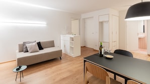 A modern, well-lit room with a sofa, a dining table with chairs, a small side table, and a cabinet with a mirror. - Modern "Hus Apartment - Nr. 4" with Balcony, Garden & Wi-Fi (Olang)