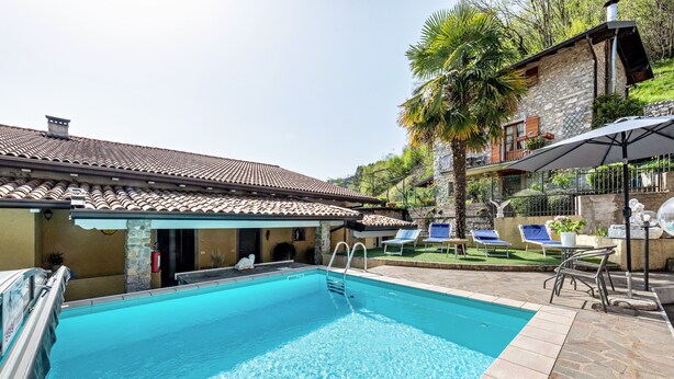A swimming pool with a tiled deck, lounge chairs, and a stone building with a tiled roof. - Beautiful Apartment “Residence Tatiana A3” with Pool, Terrace (Tremosine)