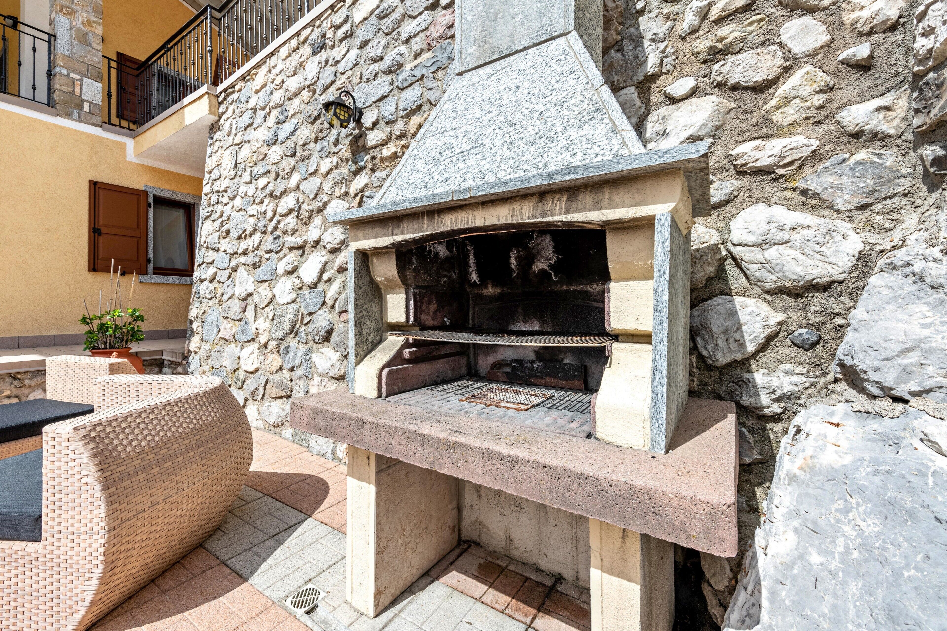 A stone-built outdoor grill area with a stone wall backdrop, a wicker sofa, and a potted plant.