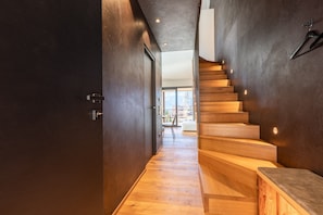 Un intérieur moderne avec un escalier en bois, des murs sombres et une vue sur l’extérieur.