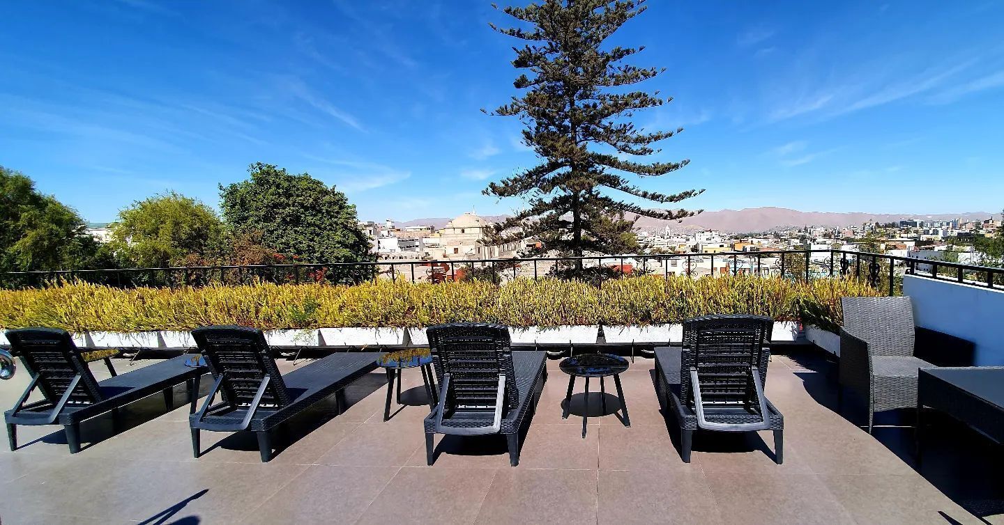 Une terrasse sur le toit, aménagée avec des chaises longues, une table et offrant une vue sur le paysage urbain, avec des montagnes à l’horizon.