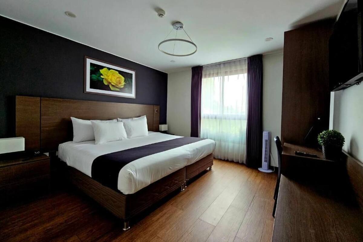 Een hotelkamer met een groot bed, houten vloeren, een wandtelevisie en een raam met gordijnen.