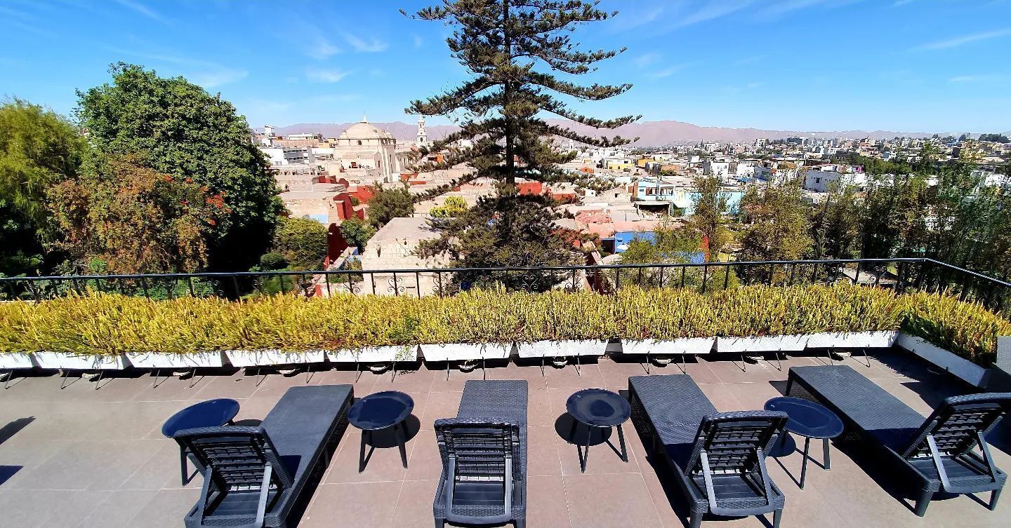 A rooftop terrace with lounge chairs and a pool, overlooking a cityscape with buildings and a mountain in the distance.