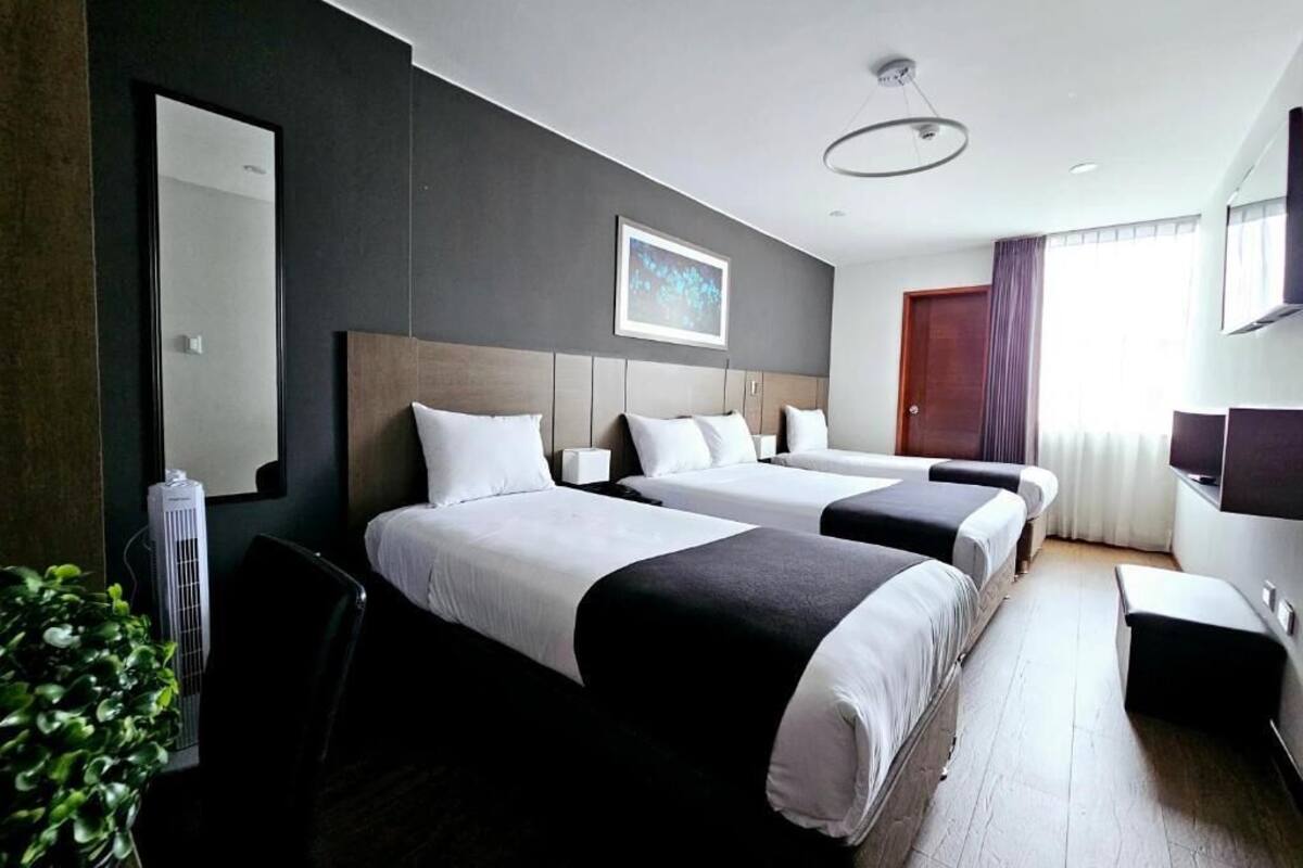 Een hotelkamer met twee bedden, een bureau, een stoel, een plant en een groot raam.