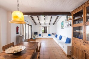 Um quarto espaçoso com uma mesa de jantar de madeira, um sofá branco com almofadas azuis, um armário de madeira e um lustre.