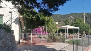 Une cour pavée de pierres, avec une clôture en métal, un espace de repos abrité et une vue sur une colline.