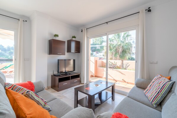 A modern living room with a sofa, a coffee table, a TV, and a sliding glass door leading to an outdoor area.