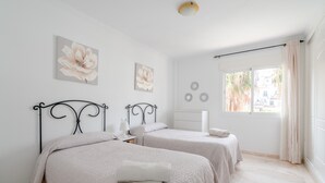 Ein Schlafzimmer mit zwei Betten, einem Fenster mit Vorhängen und Wandbildern.