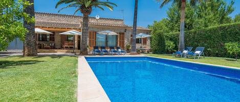 A swimming pool with lounge chairs, a patio area with umbrellas, and a stone building with a tiled roof.