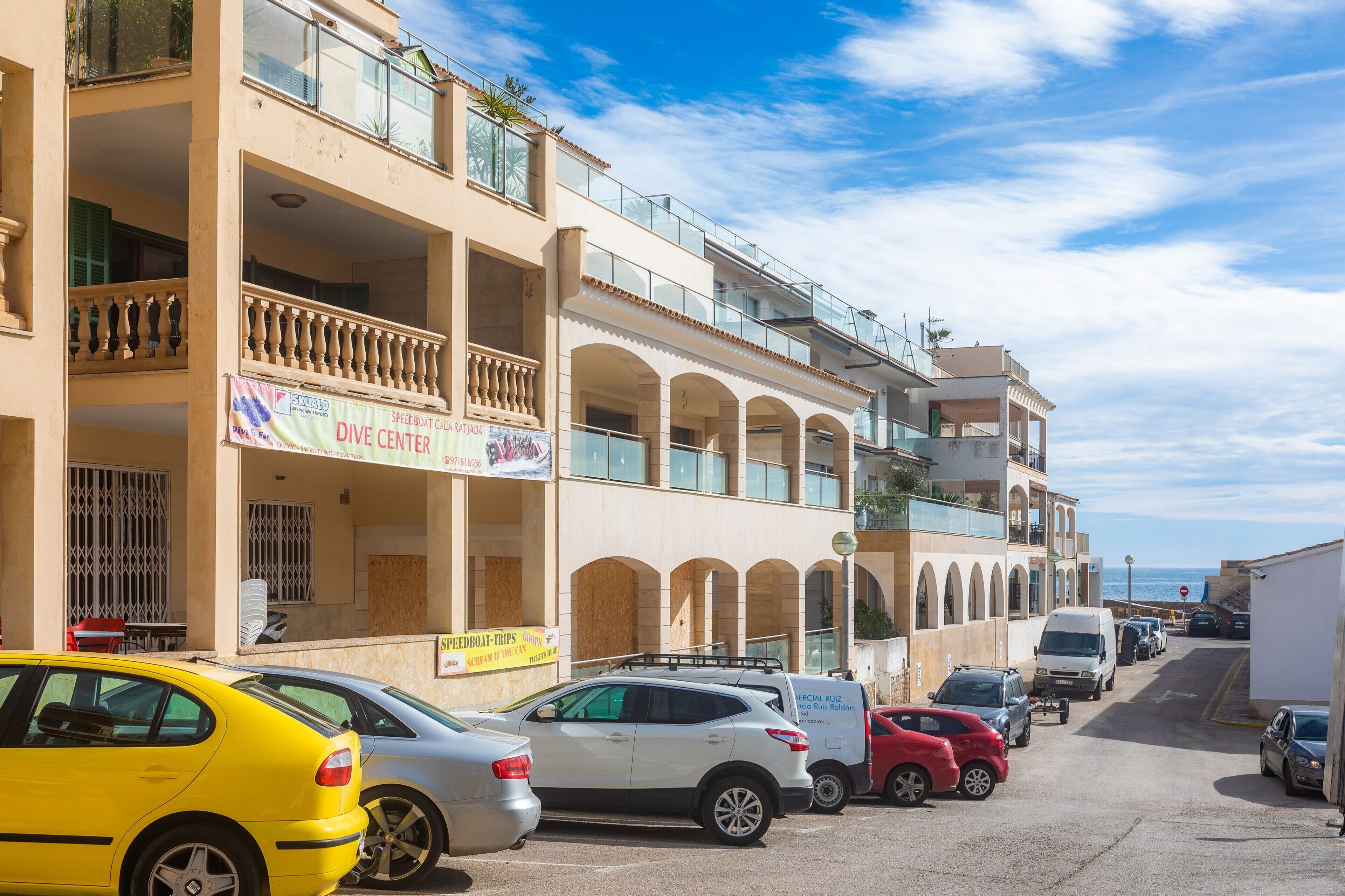 Un edificio de varios pisos con balcones, un letrero de centro de buceo y coches estacionados.