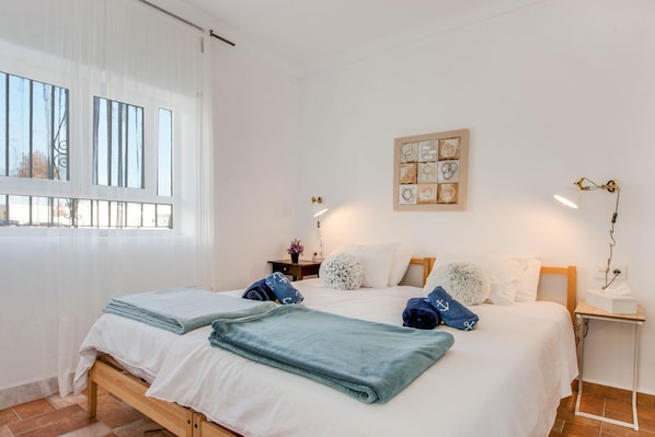 Una habitación de hotel con cama, mesita de noche, una obra de arte en la pared y ventana con cortinas.