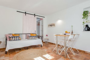 Una habitación con una cama, una mesa de comedor con sillas, una mesita auxiliar y una planta en la pared.