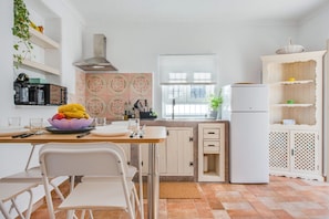 Una cocina con una mesa, sillas, un refrigerador y una ventana con persianas.