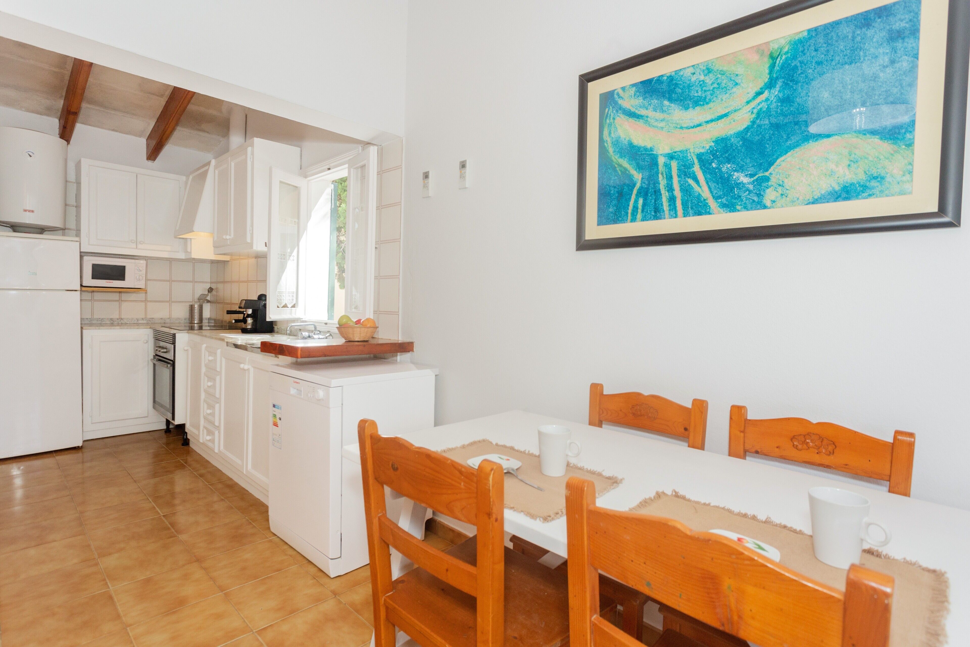 Een keuken met witte kastjes, een eettafel met houten stoelen en een lijstwerk met een schilderij aan de muur.