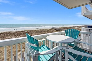 Un balcon avec vue sur la plage, une table et deux chaises.